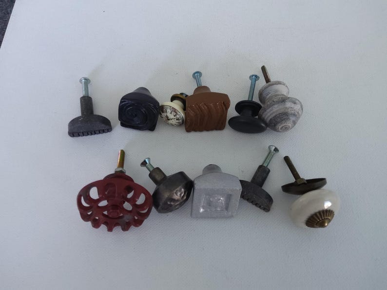 May include: Assortment of 10 decorative cabinet knobs in various styles and colours, including white, grey, brown, and black. The knobs are made of ceramic, metal, and wood.
