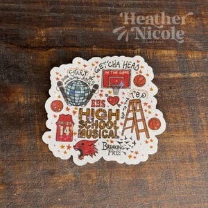May include: A white sticker with a red, orange, and yellow design. The sticker features a basketball hoop, a ladder, a basketball jersey, a disco ball, a microphone, and the text "Getcha Head in the Game", "EHS High School Musical", "Breaking Free", and "Top".