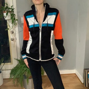 May include: Black zip-up jacket with a white, blue, and orange color block design. The jacket has a hood and a zipper closure.
