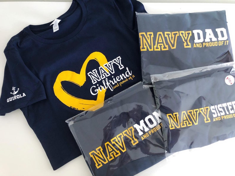 May include: Four navy blue t-shirts with yellow text and a heart design. The shirts say "Navy Girlfriend and proud of it", "Navy Dad and proud of it", "Navy Mom and proud of it", and "Navy Sister and proud of it".