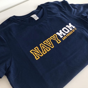 May include: Navy blue t-shirt with yellow lettering that reads "NAVY MOM AND PROUD OF IT".