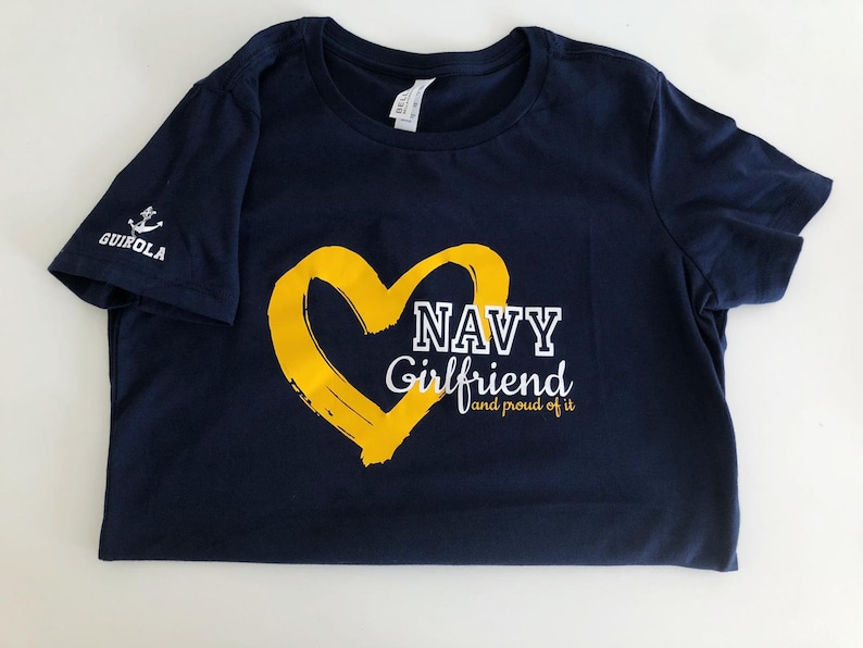May include: Navy blue t-shirt with a yellow heart and the text "NAVY Girlfriend and proud of it".