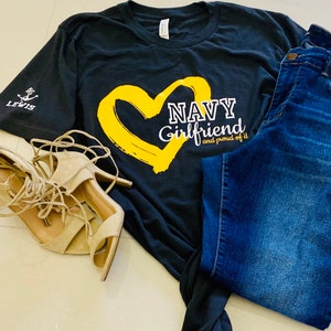 May include: A black t-shirt with a yellow heart and the text "NAVY Girlfriend and proud of it".