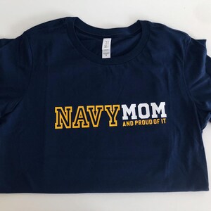 May include: Navy blue t-shirt with white text that reads "NAVY MOM AND PROUD OF IT" in yellow block letters.