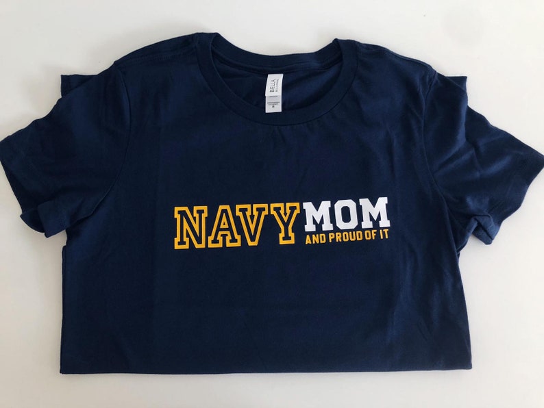 May include: Navy blue t-shirt with white text that reads "NAVY MOM AND PROUD OF IT" in yellow block letters.