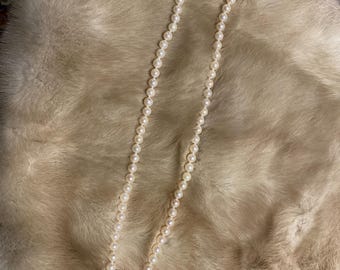 May include: A long strand of white pearls on a light brown fur background.