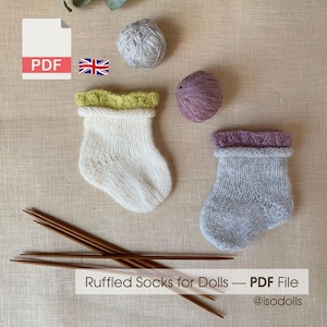 Op de afbeelding: Een PDF-bestand voor geplooide poppensokken met een witte sok met een limoengroene geplooide boord, een grijze sok met een paarse geplooide boord, twee bollen garen in grijs en paars, en vier bruine breinaalden met de tekst Ruffled Socks for Dolls.