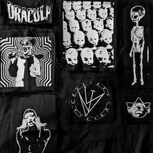 May include: A collection of black and white patches with various designs. The patches feature images of a skeleton, a screaming figure, a vampire with the word "DRACULA", and a circle with the letters "LV".