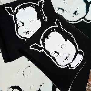 May include: Three black fabric patches featuring white images of baby dolls with devil horns. The dolls have large eyes and a creepy smile.