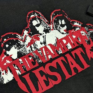May include: Black t-shirt with a red and white graphic print of three figures and the text "The Vampire Lestat".
