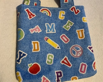 May include: A small blue denim tote bag with a colorful alphabet print. The bag has a single handle and features a rainbow, a pencil, a peace sign, and an apple.