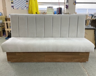 May include: A white upholstered bench with a wood base. The bench has a high back with vertical panels.