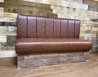 May include: Brown leather booth seating with a wood base. The booth has a curved back and a padded seat. The wood base is made of reclaimed wood planks.