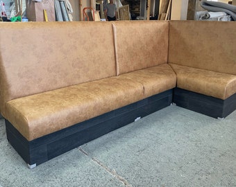 May include: A brown leather corner booth with a black wood base. The booth is in a workshop setting.