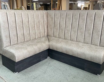 May include: A corner booth seating with a light gray fabric upholstery and a dark wood base. The booth has a high back with vertical paneling.