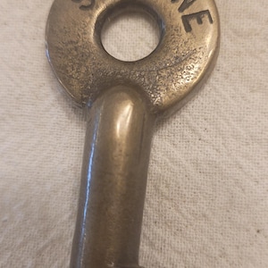 May include: Vintage brass key with the text "SOO LINE" embossed on the circular head. The key has a classic design with a long, curved stem and a rectangular bit. The key is a warm, antique brass color.