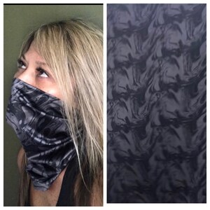 Może przedstawiać: Czarna i szara osłona twarzy z wirującym wzorem. Materiał jest narzucony na twarz, zakrywając nos i usta. Obraz pokazuje również zbliżenie wzoru materiału, który przypomina płynącą ciecz.