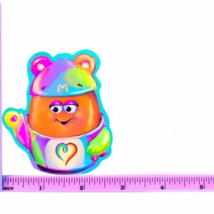 May include: A colorful cartoon character with a rainbow-colored hat and a heart on its chest. The character is wearing a blue and green outfit and has a big smile.