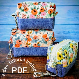 May include: Three small, square fabric pouches with floral patterns and denim blue bottoms. The pouches have silver-colored zipper pulls and key rings. The text "Video Tutorial Included PDF" is visible in the image.
