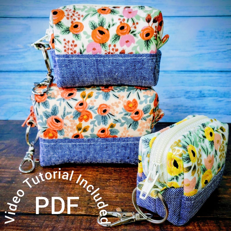 Puede incluir: Tres peque&ntilde;as bolsas de tela cuadradas con estampados florales y fondos de mezclilla azul. Las bolsas tienen cremalleras y llaveros plateados. El texto "Video Tutorial Included PDF" es visible en la imagen.
