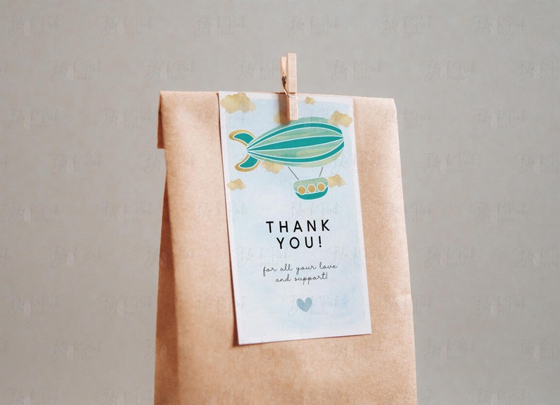 Puede incluir: Una bolsa de papel marr&oacute;n con una etiqueta de agradecimiento adjunta. La etiqueta presenta una aeronave azul y verde con detalles dorados y el texto "&iexcl;Gracias! por todo tu amor y apoyo!"