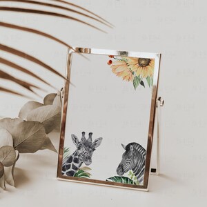 May include: A silver-framed picture featuring watercolor illustrations of a giraffe, zebra, and sunflowers. The artwork has a safari theme with green foliage and a white background. The frame is propped up on a white surface.