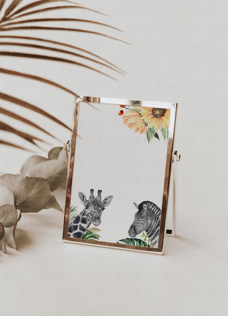 May include: A silver-framed picture featuring watercolor illustrations of a giraffe, zebra, and sunflowers. The artwork has a safari theme with green foliage and a white background. The frame is propped up on a white surface.