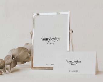 May include: A silver picture frame with a white card inside. The card has the text "Your design here!" and "5 x 7 CARD". A smaller white card with the text "Your design here!" and "2 x 3.5 CARD" is sitting in front of the frame. A sprig of eucalyptus is on the left side of the frame.