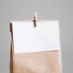 May include: A brown paper bag with a white card attached to the top with a wooden clothespin. The card is blank.