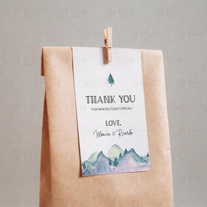 Puede incluir: Una etiqueta de agradecimiento con una ilustraci&oacute;n de acuarela de monta&ntilde;as y un pino. El texto dice "Gracias por hacer que este d&iacute;a sea especial! Con amor, Monica & Ricardo."
