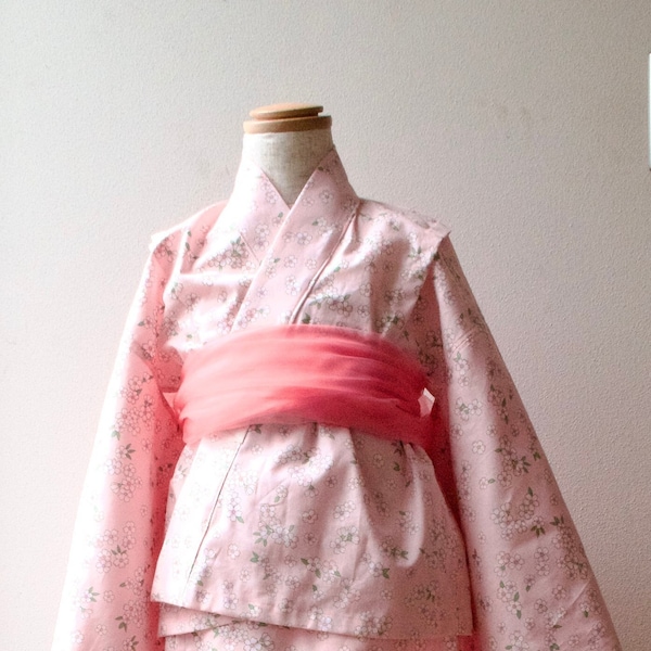 Smiling anime girl in a pink and yellow kimono among cherry blossoms on