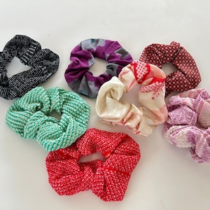 May include: Eight colorful scrunchies made from fabric with different patterns. The scrunchies are in various colors, including red, green, purple, white, and black.