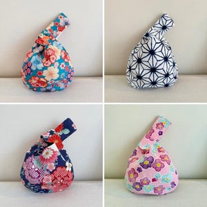 May include: A collection of four Japanese knot bags, each with a different pattern. The bags display floral and geometric designs in shades of blue, pink, and white. The knot bags are tied at the top, showcasing their unique style.