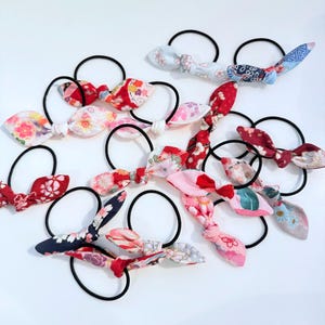 Puede incluir: Una colección de cintas para el pelo de colores con lazos de tela. Los lazos están hechos de varias telas estampadas, incluyendo diseños florales y geométricos. Las cintas para el pelo son negras y elásticas.