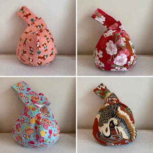Puede incluir: Cuatro bolsas de nudo japonesas con varios diseños. Una es rosa con ilustraciones de perros marrones, otra es roja con diseños florales blancos y rosas, una tercera es azul con diseños florales y la última es roja con un diseño de grulla.