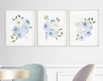 May include: Three framed watercolor prints of blue and white floral bouquets. The prints are displayed on a white wall above a dining table with two chairs.