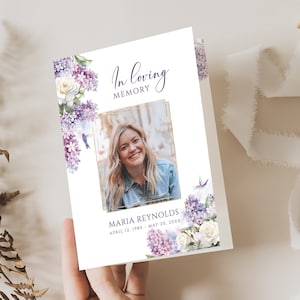 Könnte beinhalten: Eine weiße Gedenkkarte mit einem goldenen Rahmen um ein Foto einer Frau. Die Karte hat ein lila-weißes Blumenmuster mit dem Text "In liebevoller Erinnerung" und "Maria Reynolds, 12. April 1980 - 20. Mai 20XX".