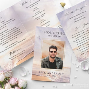 Op de afbeelding: Een programma voor een herdenkingsdienst met een foto van een man met een zonnebril. Het programma heeft een aquarel achtergrond met een strandscène en de tekst "Honoring the Life of Rick Anderson 1975 - 2025".