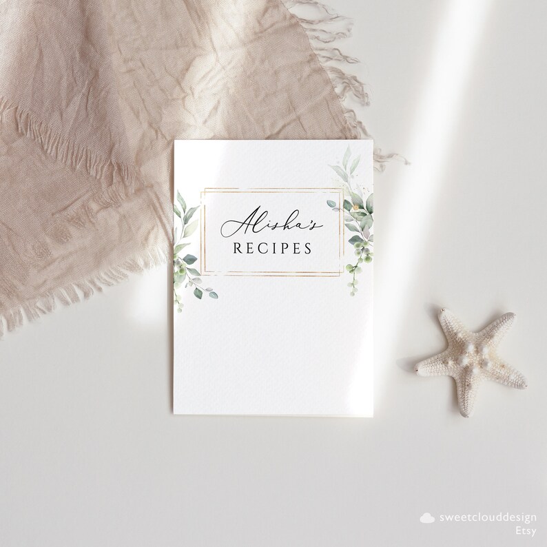 May include: A white recipe book cover with a gold frame and green foliage. The text "Alisha's Recipes" is written in black cursive font.