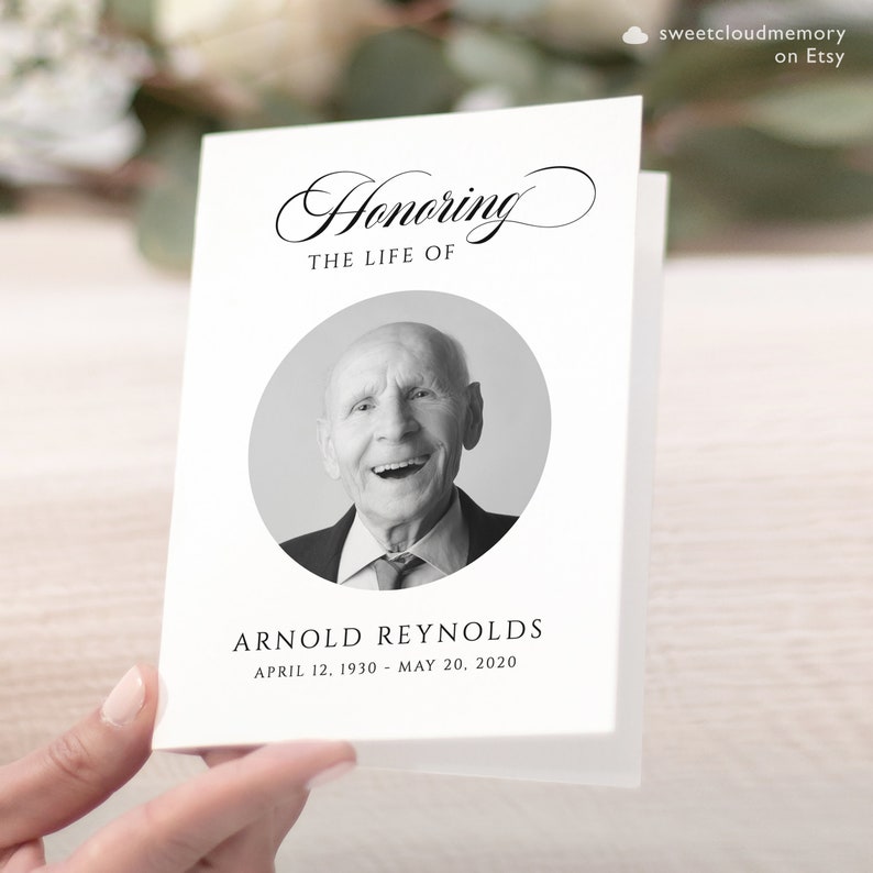 May include: A black and white photo of a man smiling, in a circle on a white card. The card says "Honoring The Life Of Arnold Reynolds April 12, 1930 - May 20, 2020".