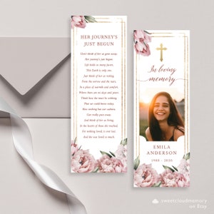 Puede incluir: Un marcapáginas conmemorativo rosa y dorado con un diseño floral y una foto de una mujer sonriente. El texto dice "Her Journey's Just Begun" y "In loving memory". El nombre de la mujer es Emila Anderson y las fechas son 1980-2020.