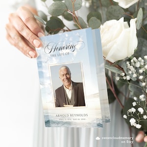 May include: A blue and white funeral program with a photo of a man in a suit. The program has the text "Honoring the Life of Arnold Reynolds April 12, 1970 - May 20, 2030".