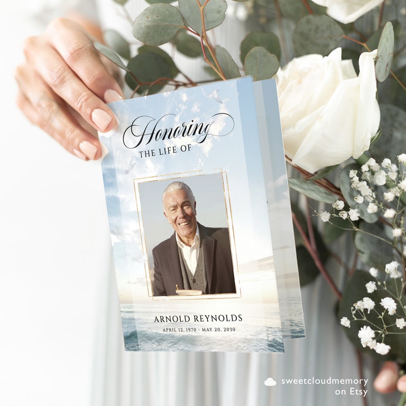 May include: A blue and white funeral program with a photo of a man in a suit. The program has the text "Honoring the Life of Arnold Reynolds April 12, 1970 - May 20, 2030".