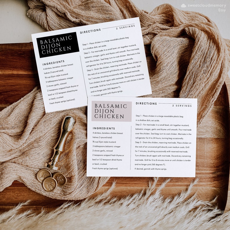 May include: Two recipe cards for Balsamic Dijon Chicken. The cards are on a wooden surface with a beige fabric underneath. The cards are printed with black text on a white background. The ingredients and directions are listed for making the chicken.