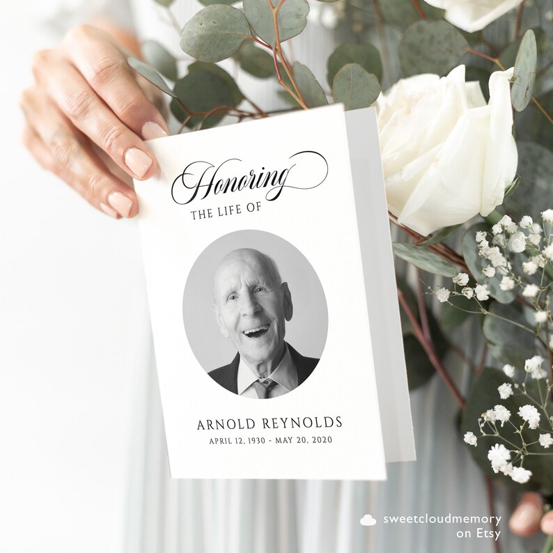 May include: A black and white photo of a man smiling, with the text "Honoring the Life of Arnold Reynolds April 12, 1930 - May 20, 2020" on a white card.