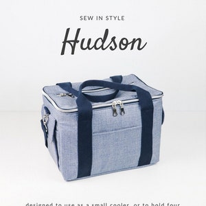 May include: A blue and black fabric tote bag with a zipper closure and two handles. The bag is designed to be used as a small cooler or to hold four plastic storage boxes. The bag is labeled "Hudson" and is a sewing pattern from Sallie Tomato.