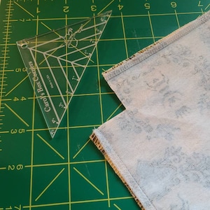 May include: A green cutting mat with a clear plastic ruler labeled "Carol's Box Corners" and a piece of fabric with a floral pattern.