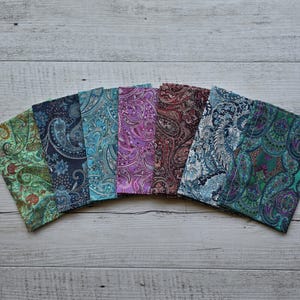 Może przedstawiać: Zestaw siedmiu próbek tkaniny z wzorami paisley w różnych kolorach, w tym zielonym, niebieskim, fioletowym i czerwonym.