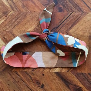 Puede incluir: Una diadema de color marrón, azul, rosa y blanco con un diseño anudado.