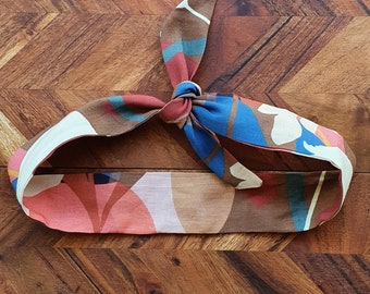 May include: A brown, blue, pink, and white patterned headband with a knotted design.